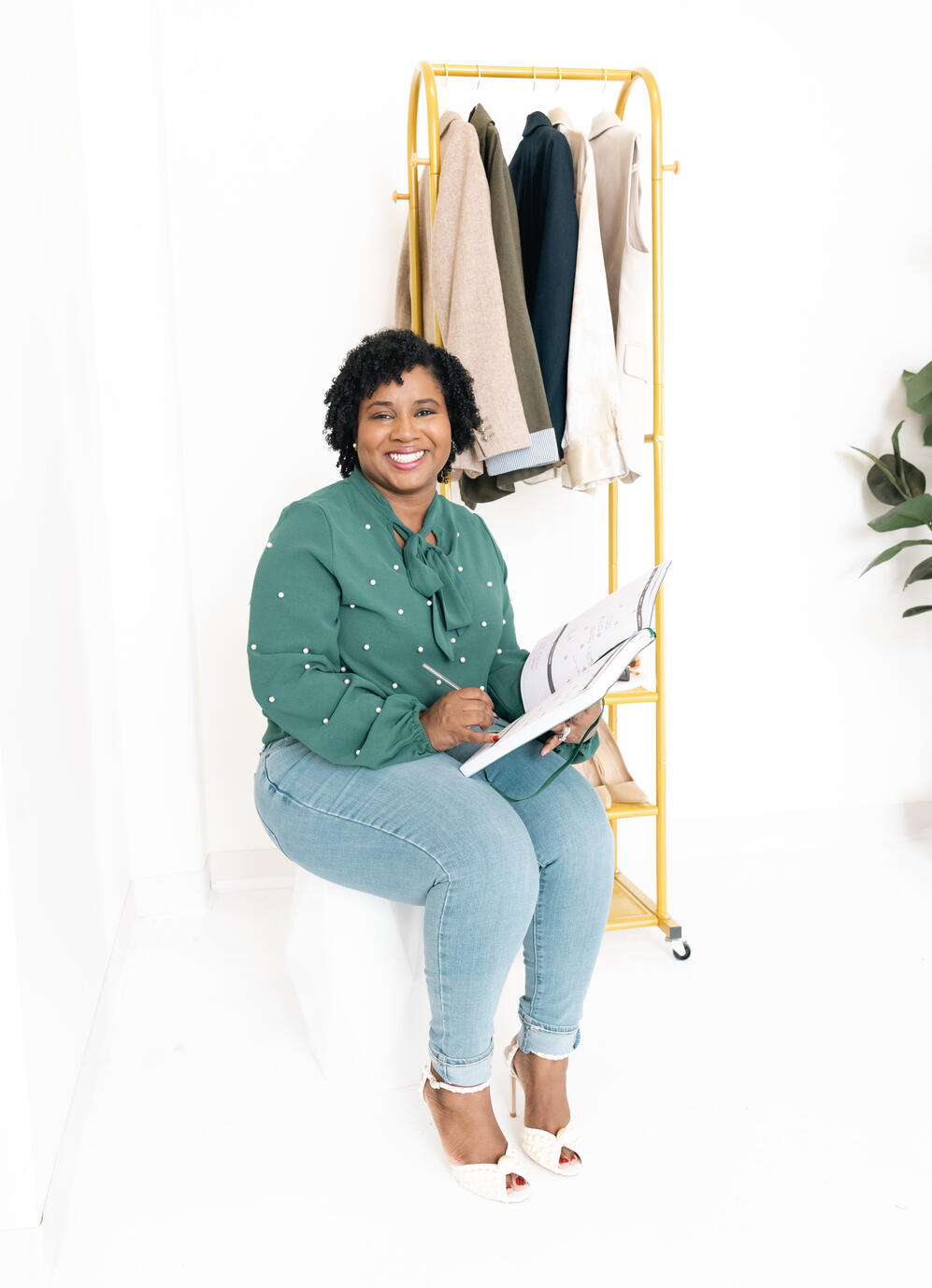 Bria Johnson seated in a green top and jeans, smiling during a brand portrait session.