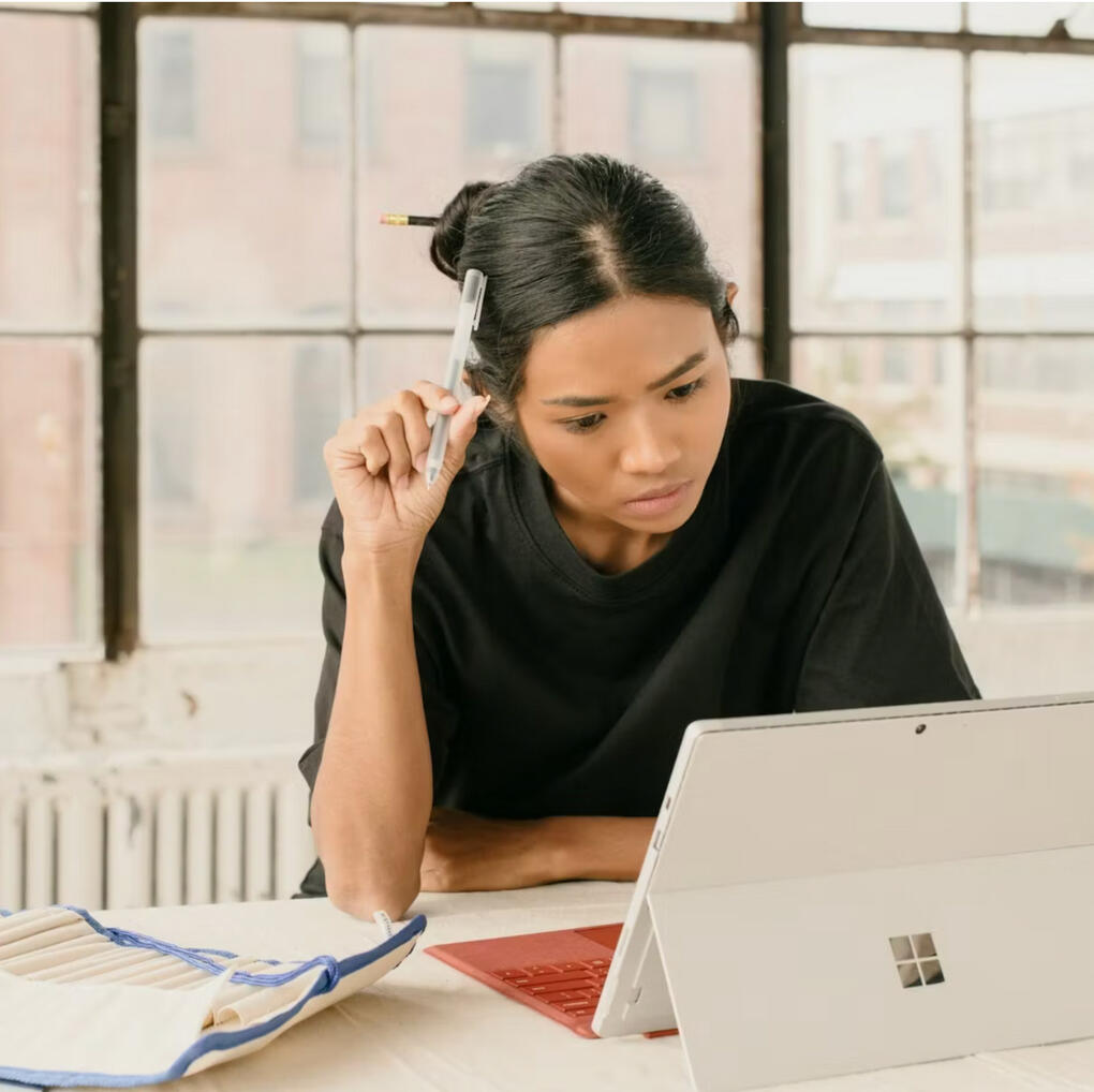 The Gal Project — Founder Feature Woman sitting at a desk, looking at a laptop while holding a pen to her head, used as the thumbnail for a founder feature article.